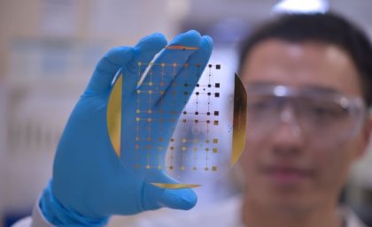Quan Zhou holds up the device his laboratory is using to explore faster, more accurate methods of diagnosis. Image: The University of Queensland. A close up image of a slide showing tiny rectangles, held up by the gloved hand of a researcher who is out of focus.